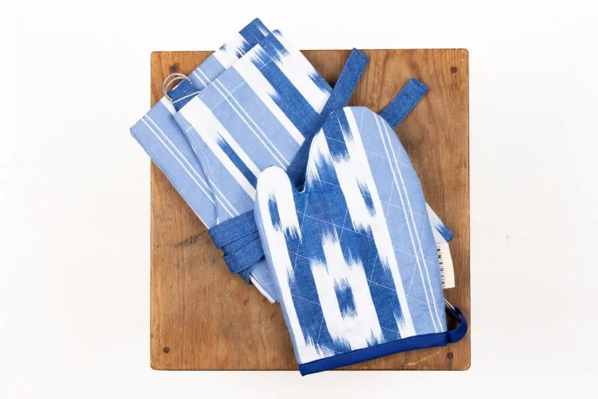 Set de cocina con guante y paño de tela ikat mallorquín azul con patrón geométrico sobre fondo blanco, presentado sobre tabla de madera