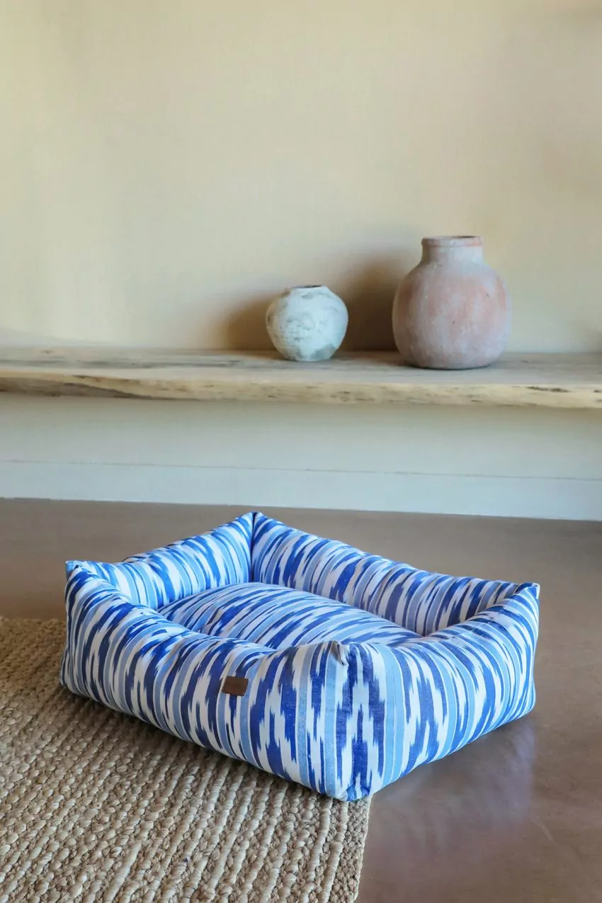 Cama para mascotas con tejido mallorquín azul y blanco de Teixits Vicens, colocada sobre alfombra de yute