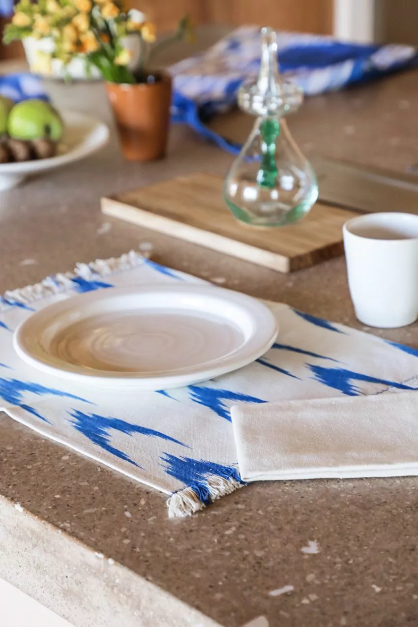 Mantel individual con estampado azul tipo ikat, acompañado de vajilla blanca