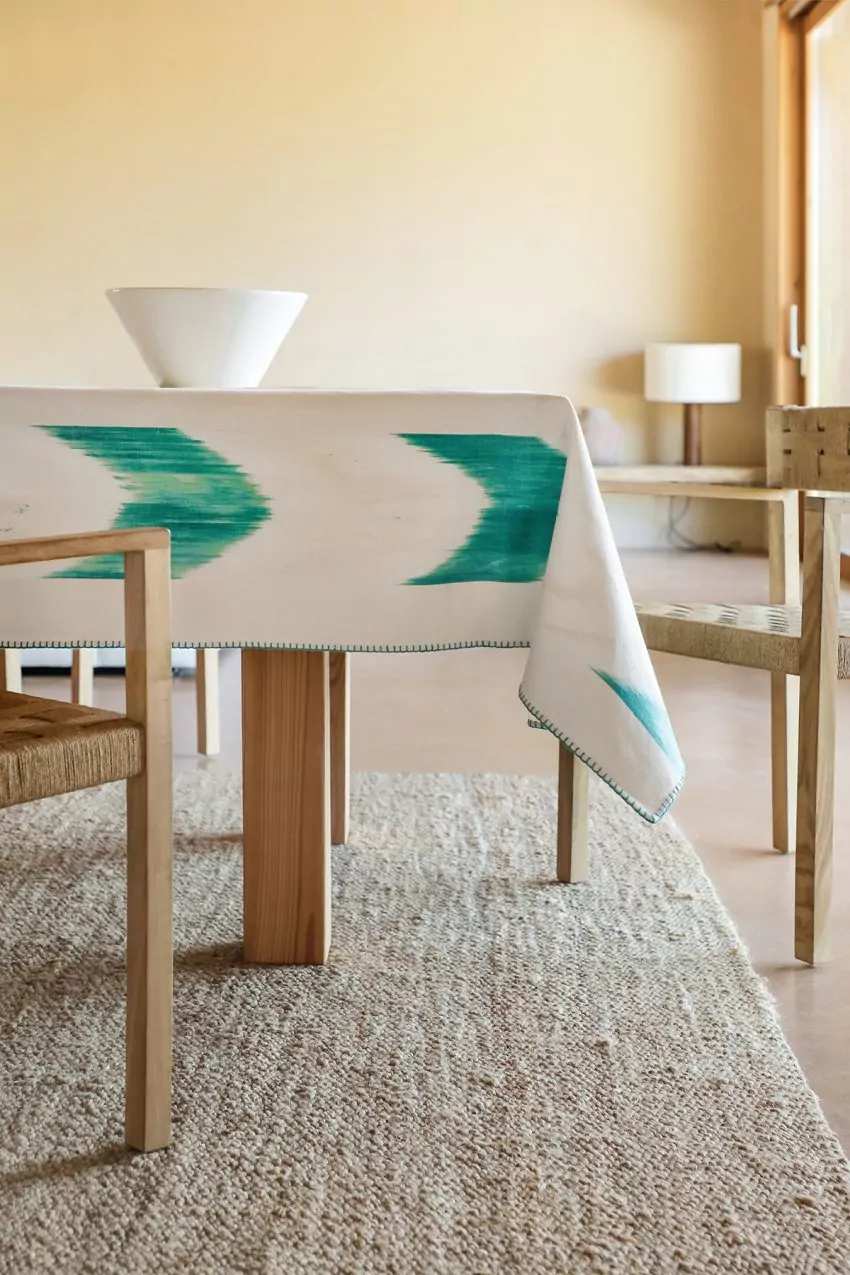 Mantel blanco con estampado ikat en verde turquesa colocado en una mesa de comedor de madera clara
