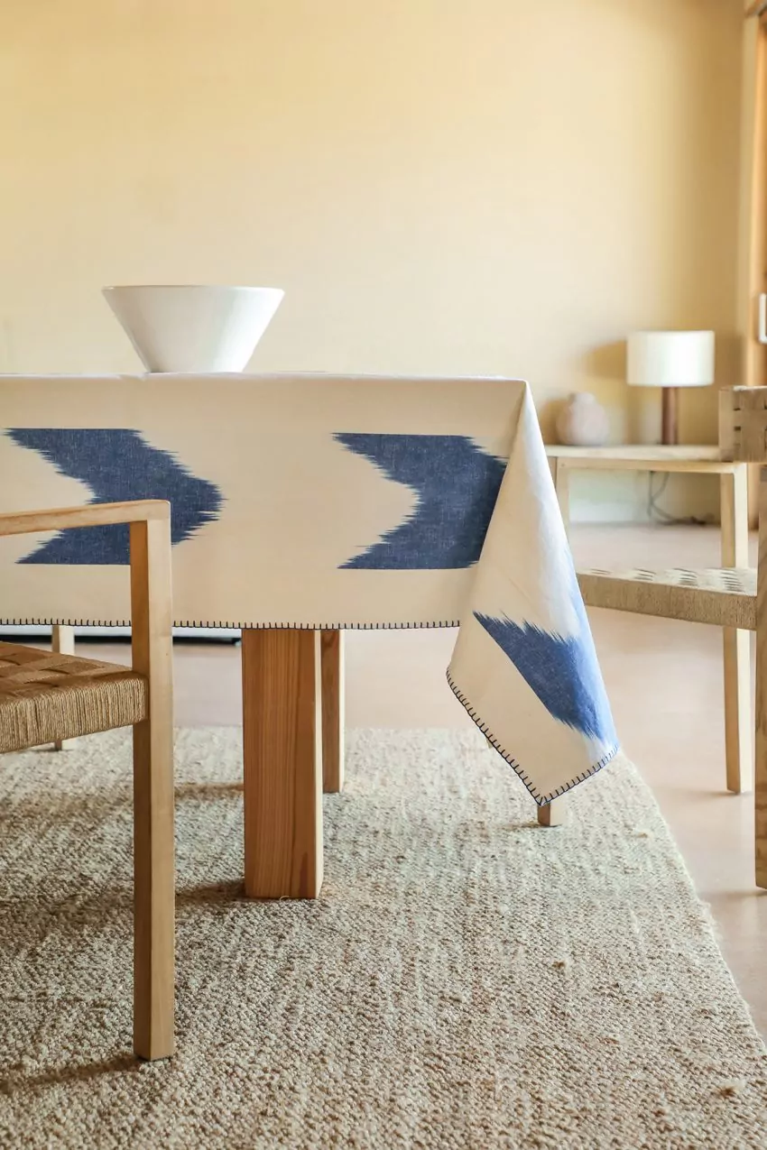 Mantel blanco con patrón azul ikat sobre mesa rústica y sillas de madera trenzadas